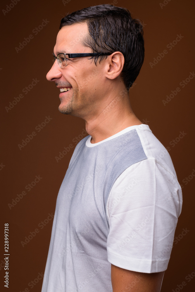 Profile view portrait of handsome man smiling against brown background Profile view portrait of handsome man smiling against brown background