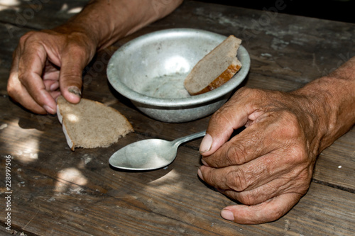 Hands the poor old man's, piece of bread and empty bowl on wood background. The concept of hunger or poverty. Selective focus. Poverty in retirement.Homeless. Alms