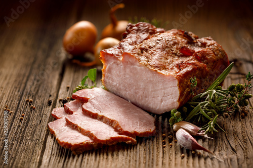 Smoked meats, sliced smoked pork loin on a wooden  table with addition of fresh  herbs and aromatic spices.  Traditional smoked meat smoked in apple  and beech  wood, Natural product from organic farm