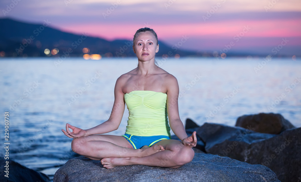 Sportwoman meditating in yoga padmasana in evening