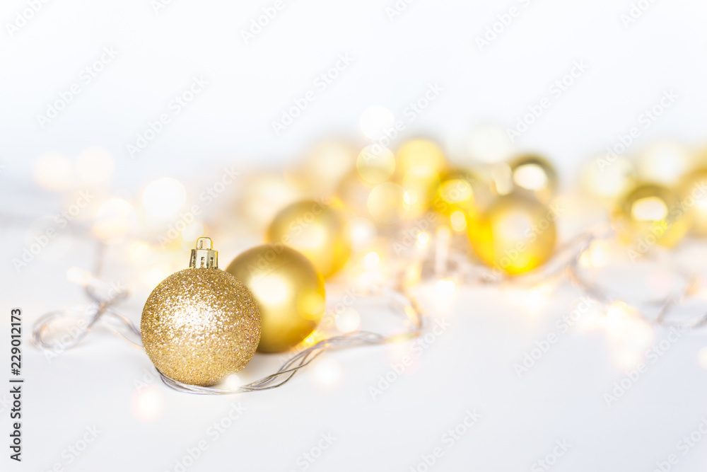 Christmas lights in warm yellow white on string and gold xmas balls over light  background with