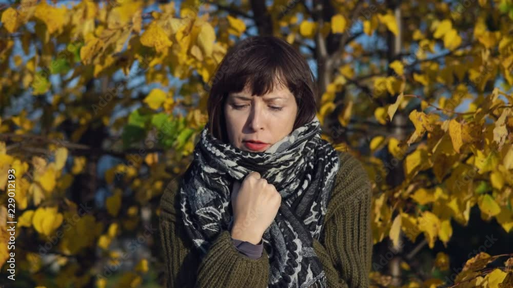 A young woman in a green knitted sweater is wrapped in a warm scarf against the yellow foliage in the city Park in the Indian summer.