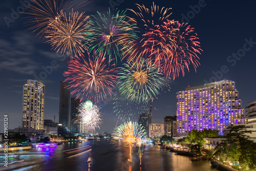 New Year Fireworks at midnight over clear sky above river city surrounding with luxury hotels, restaurants, condominiums, shopping mall in main city for special happy holiday celebration event