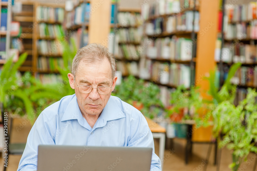Old man using laptop in library. Empty space for text Old man using laptop in library. Empty space for text