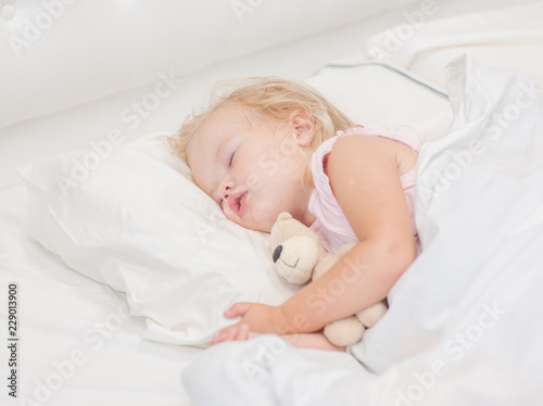 little baby girl sleeping on a bed with toy bear