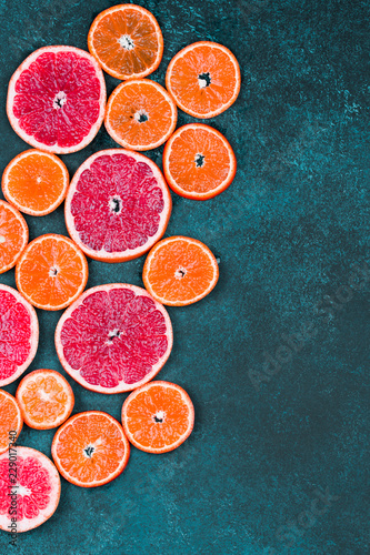 Fresh oranges, grapefruits and madarine slices on dark stone background.