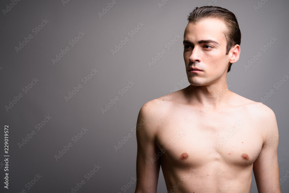 Young handsome man shirtless thinking and looking up against gray background Young handsome man shirtless thinking and looking up against gray background