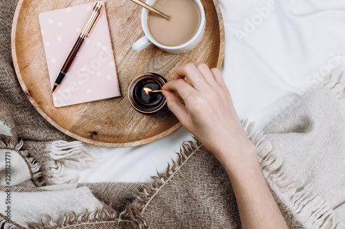 Cozy flatlay with wooden tray, cup of coffee or cocoa, candle, notebooks on white sheets and blankets photo