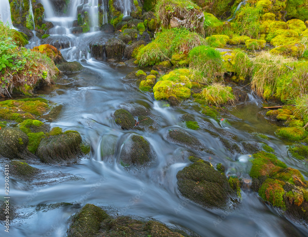 Wasser fliesst im Bach zwischen Felsen mit grünem Moss Wasser fliesst im Bach zwischen Felsen mit grünem Moss