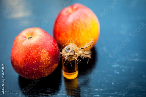 Close up of organic concentration or essence of apple or Malus or seb in a transparent bottle with raw apple on wooden surface. photo