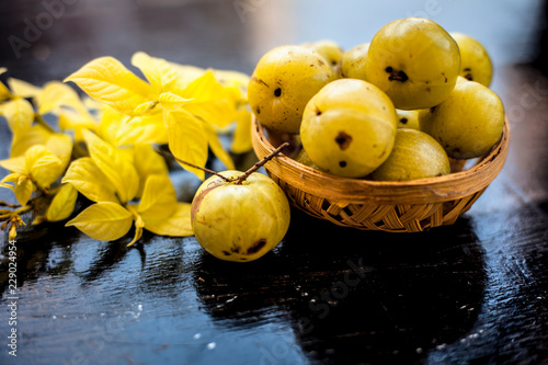 Close up of organic raw Indian gooseberry or amla or Ribes uva-crispa in a vegetable and fruit basket made up of bamboo on wooden surface with some leaves of Rangoon's creeper. photo