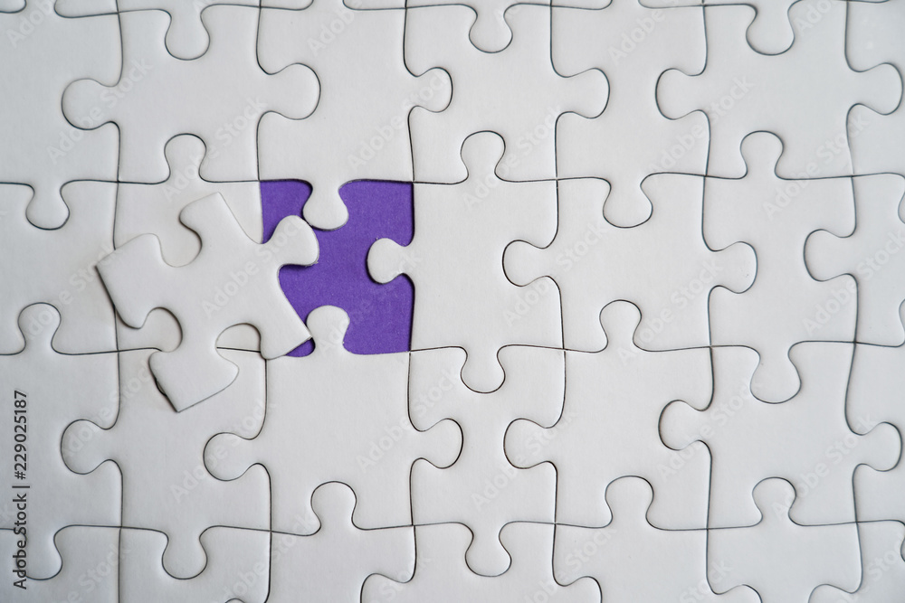 Fragment of a folded white jigsaw puzzle and a pile of uncombed puzzle elements against the background of a Violet surface. Fragment of a folded white jigsaw puzzle and a pile of uncombed puzzle elements against the background of a Violet surface.