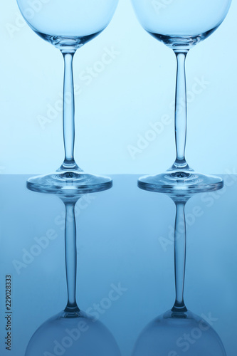 Two wine glasses on reflective surface. Close up. Blue lighting.