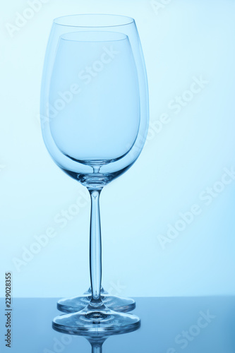 Two empty wine glasses standing together. Blue lighting.
