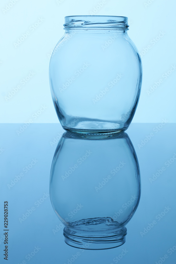 Round shape glass jar. Opened empty utensil. Reflective surface. Round shape glass jar. Opened empty utensil. Reflective surface.