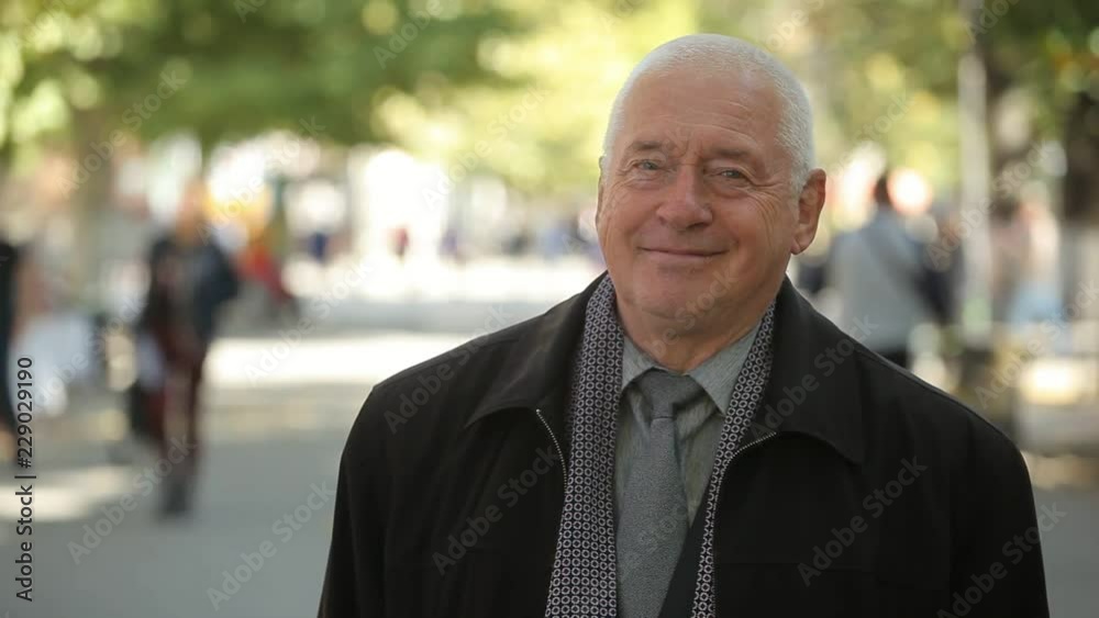  Cheerful portrait of a white haired man in a clean coat, scarf, shirt and necktie smiling happily  in a green street in autumn.    