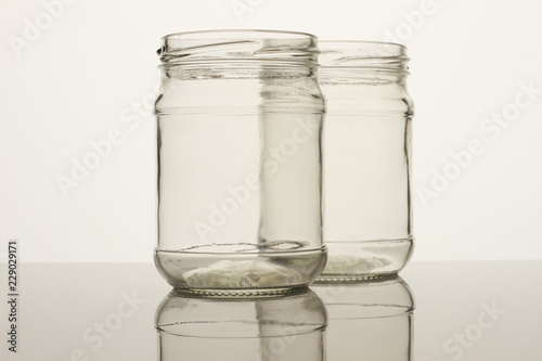 Two glass transparent empty jars. White background. Reflective surface.