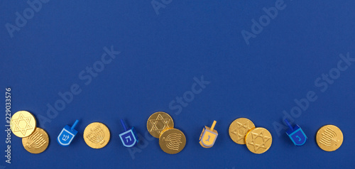 Dark blue background with multicolor dreidels and chocolate coins at the bottom. Hanukkah and judaic holiday concept.