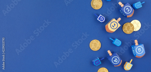 Dark blue background with multicolor dreidels and chocolate coins on the right. Hanukkah and judaic holiday concept.