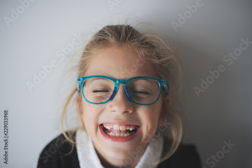 funny delightful face of little laughing caucasian girl in blue glasses