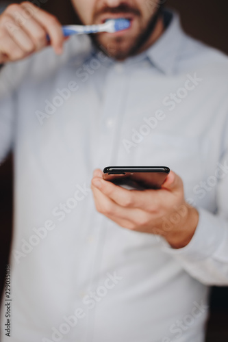 close up of man using smartphone. concept of phone addiction. young business man typing and browsing social media on his phone while brushing his teeth. 