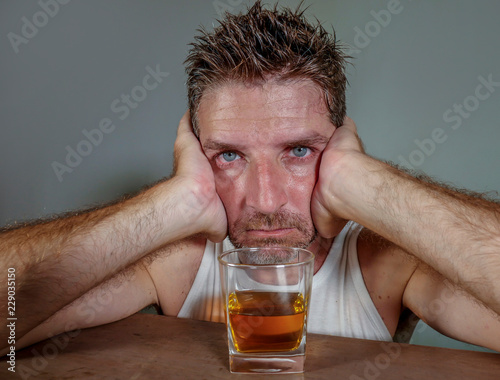 young wasted and depressed alcohol addict man in dirty singlet drinking glass of whiskey feeling desperate suffering alcoholism problem and booze addiction in alcoholic concept