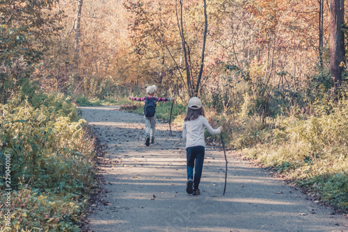 Little boy and girl with wooden sticks in their hands wallking along the trail in the autumn forest, the concept of friendship and adventure