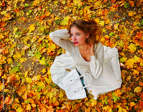 Autumn fashion women high-grade long sleeve feminity lace dress with long sleeve below knee in princess style. Top view of woman dramatic look sitting on fall leaves in city park outdoor.