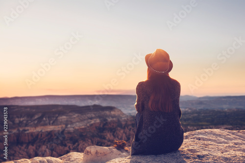 A girl in a hat on top of a hill in silence and loneliness admires a tranquil natural landscape in search of a soul.