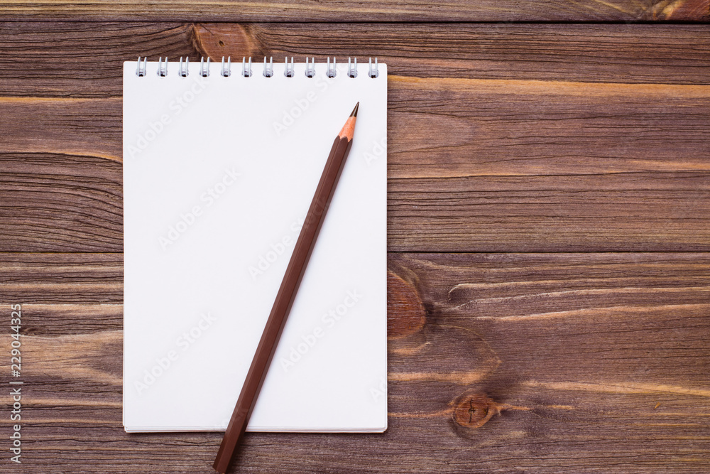 Clean open notepad for writing on a spiral mount sheet and brown pencil on a wooden background. Top view. Copy space Clean open notepad for writing on a spiral mount sheet and brown pencil on a wooden background. Top view. Copy space