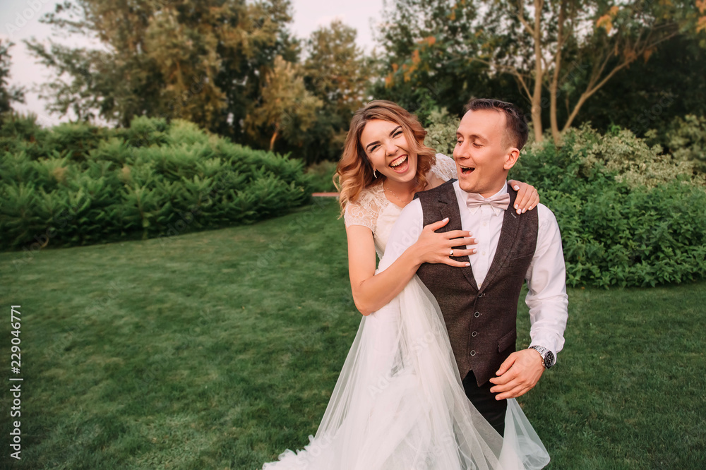 a lovely young couple, a bride wearing a long light white wedding dress and a groom in a gorgeous green garden. a girl embraces her man, laughing in an amazing garden, emotional wedding photo