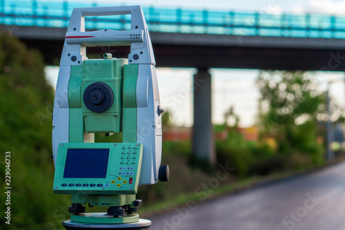 Surveyor equipment (theodolit or total positioning station) on the construction site of the motorway or road with bridge in background