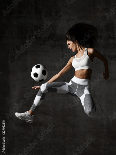 Woman player run jump and hit soccer ball yelling screaming with dust splashes