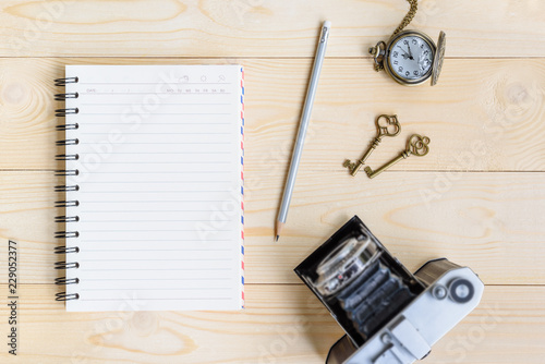 Top view from above / flat lay of blank page spiral or flipped notepad / opened diary book, old retro 35mm film camera, 2 vintage keys, a watch, a pencil on wood table, for writing plan, schedule etc © William W. Potter