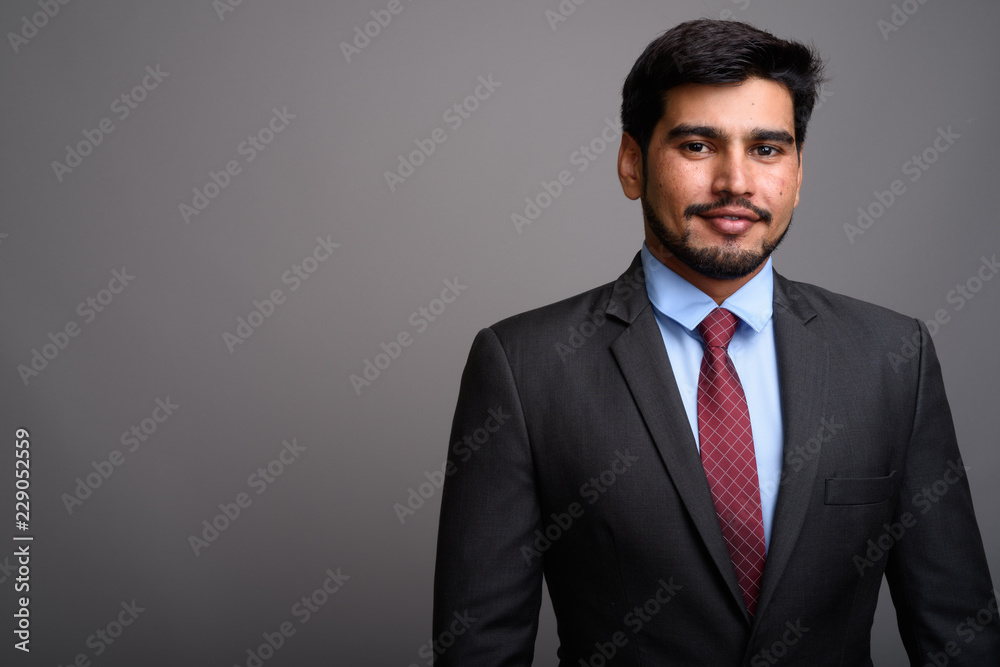 Young handsome bearded Persian businessman against gray backgrou Young handsome bearded Persian businessman against gray backgrou