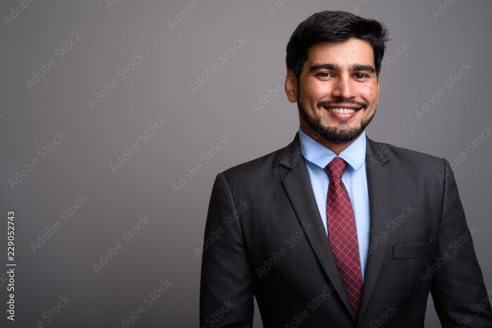 Young handsome bearded Persian businessman against gray backgrou Young handsome bearded Persian businessman against gray backgrou