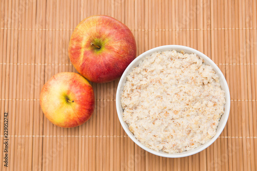 Oatmeal in white bowl and red apple on white background. Isolated on white. Healthy food