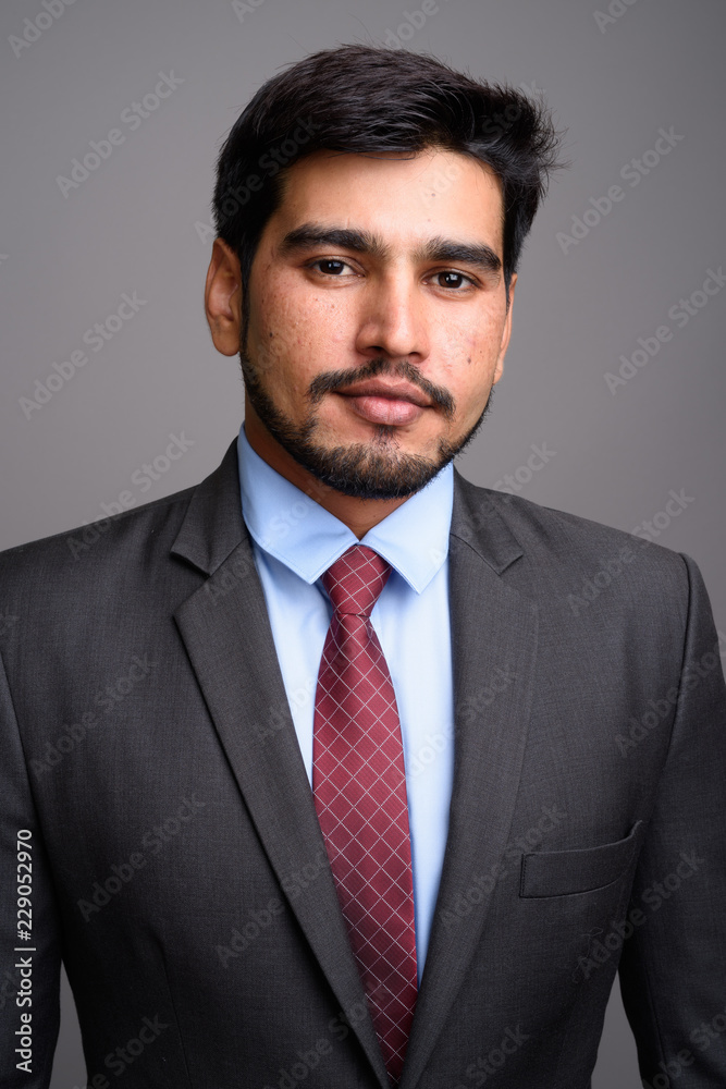 Young handsome bearded Persian businessman against gray backgrou Young handsome bearded Persian businessman against gray backgrou