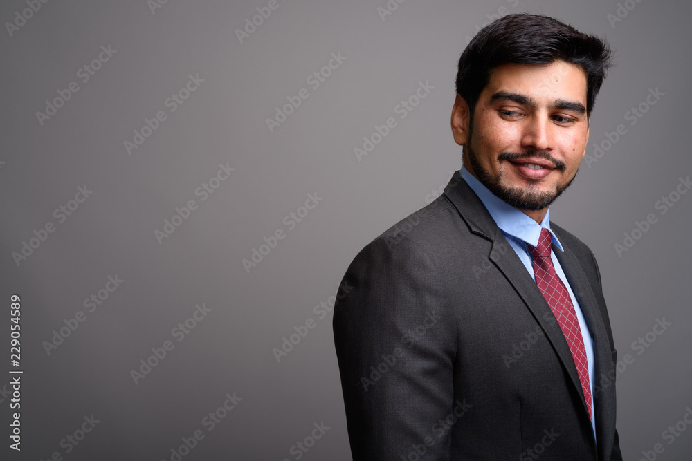 Young handsome bearded Persian businessman against gray backgrou Young handsome bearded Persian businessman against gray backgrou