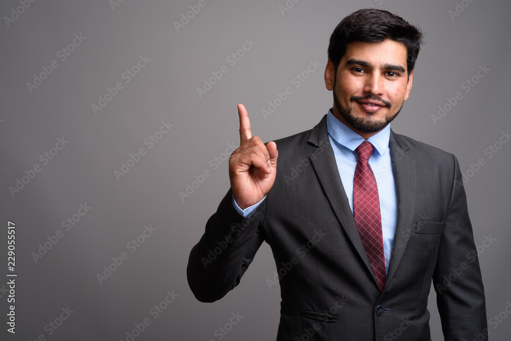 Young handsome bearded Persian businessman against gray backgrou