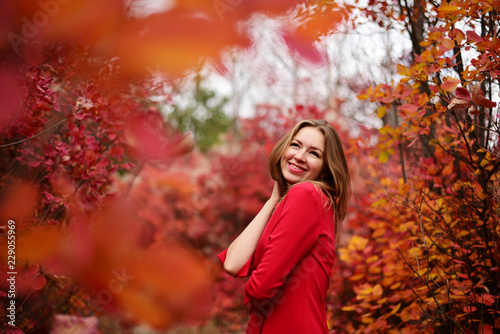Beautiful cheerful girl in a red dress in the autumn park