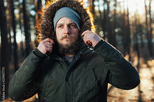 close up portrait of a bearded hipster tourist in gray hood man in the sunlight