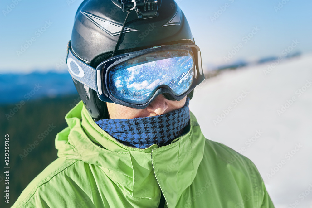 Close up of the ski goggles of a man with the reflection of snowed mountains. A mountain range reflected in the ski mask. Man on the background blue sky. Wearing ski glasses. Winter Sports. Close up of the ski goggles of a man with the reflection of snowed mountains. A mountain range reflected in the ski mask. Man on the background blue sky. Wearing ski glasses. Winter Sports.