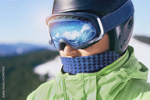 Close up of the ski goggles of a man with the reflection of snowed mountains.  A mountain range reflected in the ski mask.  Portrait of man at the ski resort on the background of mountains and sky