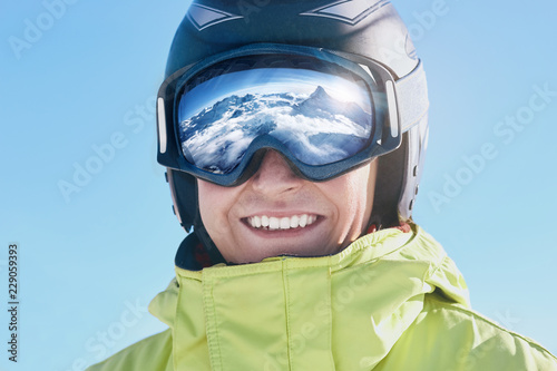 Close up of the ski goggles of a man with the reflection of snowed mountains.  A mountain range reflected in the ski mask.  Portrait of man at the ski resort.  Wearing ski glasses. Winter Sports.