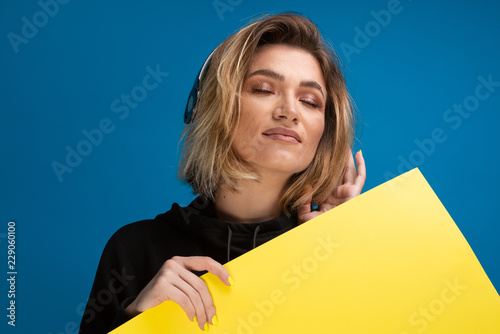 Portrait of girl with headphones and eyes closed, enjoying music while holding a card baord. Copy space for displaying ads photo