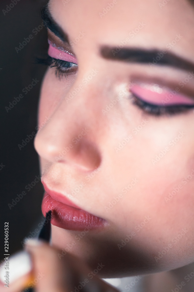 Hand of make-up master, painting lips of young beautiful model.