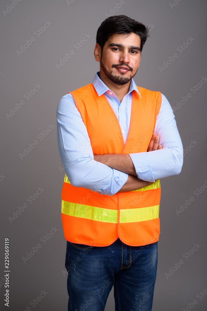 Fototapeta premium Young handsome bearded Persian man construction worker against g