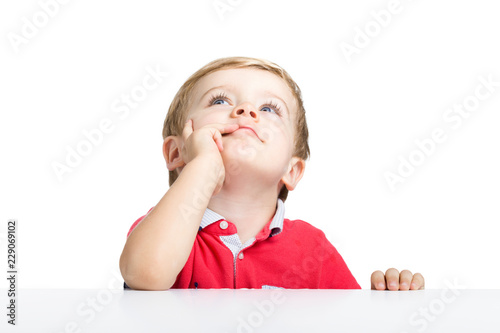 Llittle boy standing at white table looking up, isolated on a white background