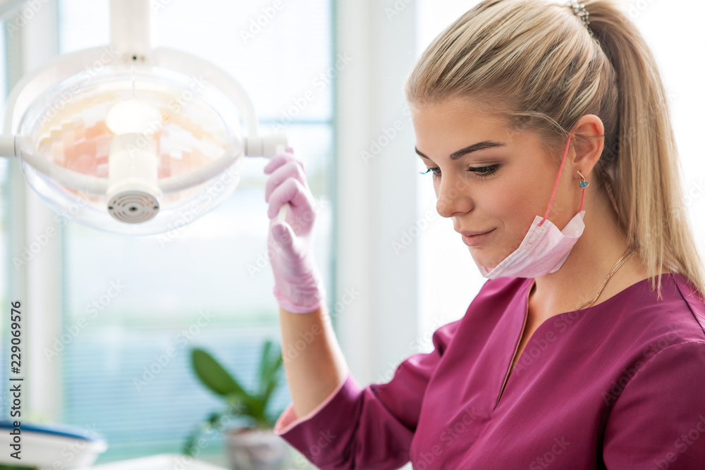 Woman dentist holding lamp and lookinf for a patient in dental office